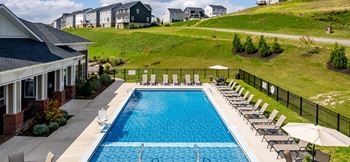 A swimming pool in front of a house with a hill behind it